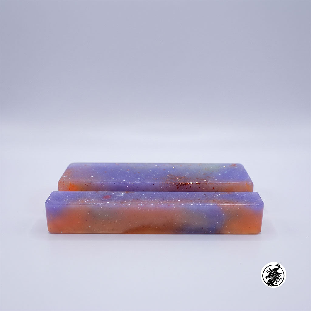 Two rectangular resin bars with a marbled purple, orange, and blue galaxy pattern, speckled with white glitter, displayed on a light gray background.