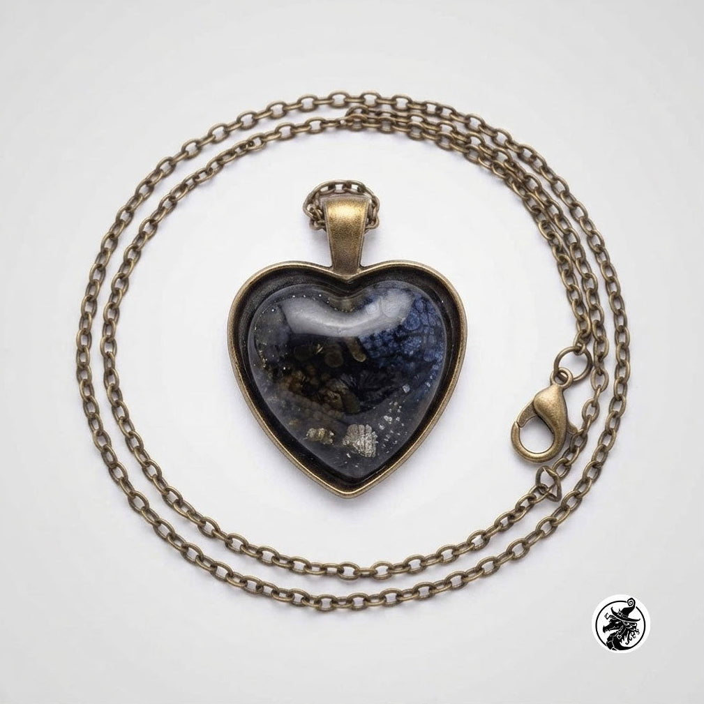 A heart-shaped glass pendant necklace with a dark blue and black marbled design inside, set in an antique bronze-toned metal frame, on a matching chain with a lobster clasp, photographed on a light gray background.
