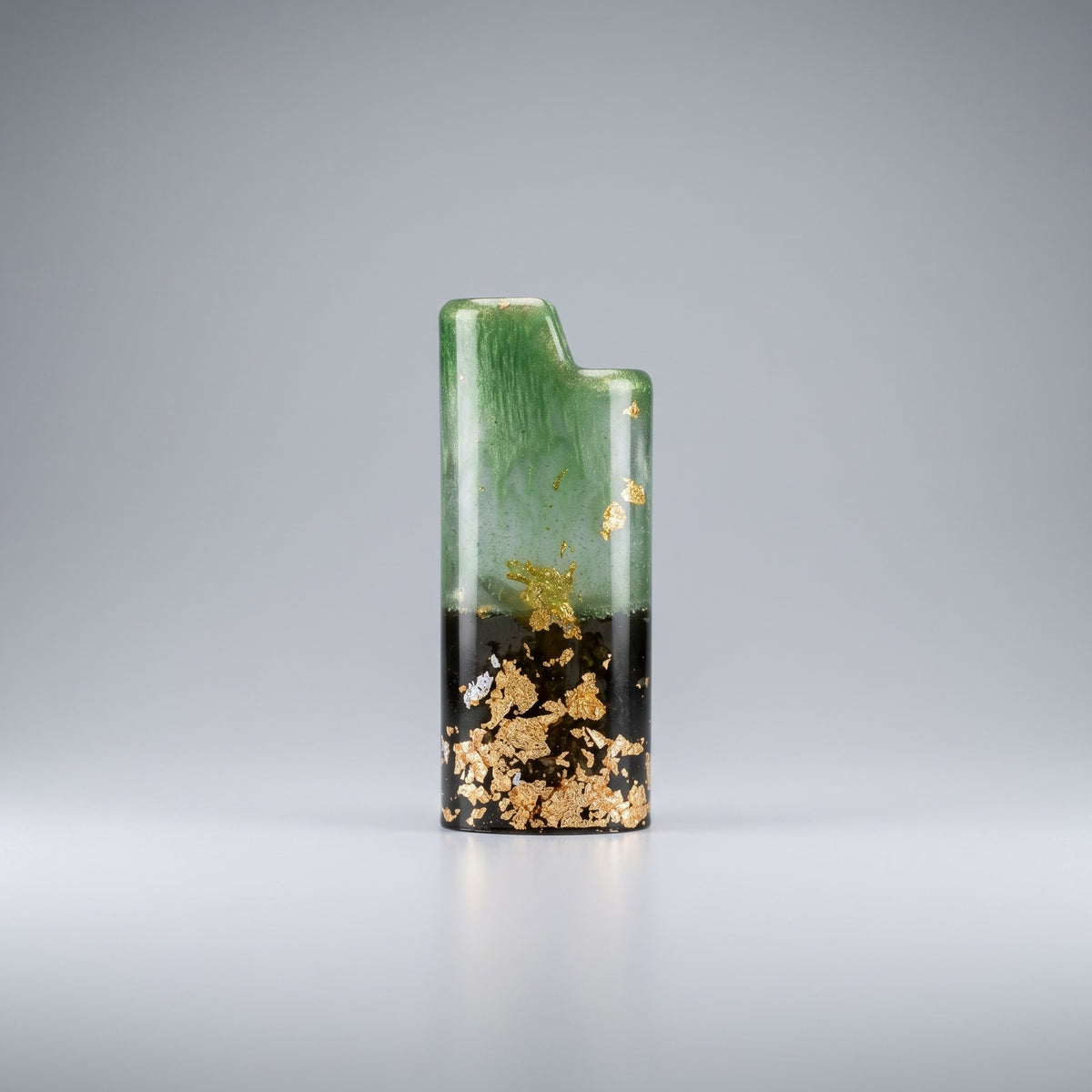 Handcrafted resin lighter case with emerald green swirls, a black base, and embedded gold leaf flakes on a metal pedestal.