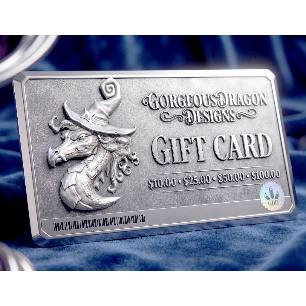 A rectangular metallic gift card from Gorgeous Dragon Designs featuring an embossed dragon wearing a witch hat, displayed on a dark blue velvet fabric background.