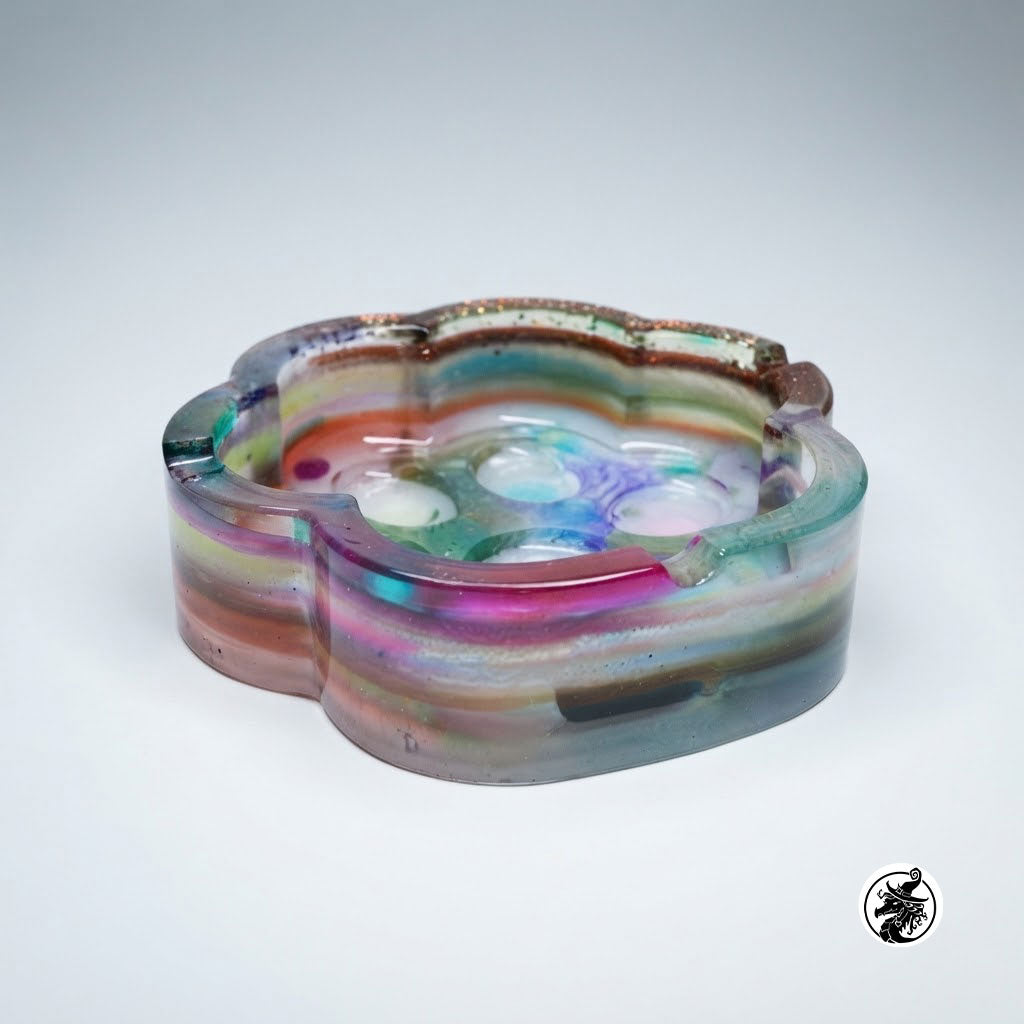 A translucent resin tray with a flower-like scalloped edge, filled with layered iridescent bands of pink, purple, blue, green, and brown, photographed on a light gray studio background.