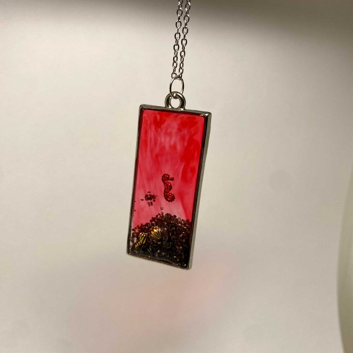 Rectangular pendant with red and black design on a chain against a neutral background
