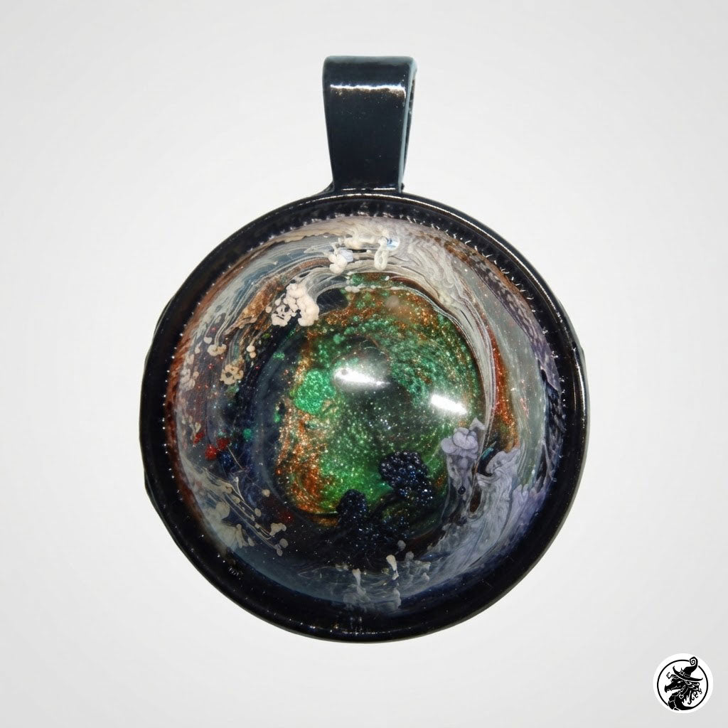 A round pendant with a black metal border and bail, featuring a colorful resin or glass center with swirling green, gold, white, and dark blue patterns, shown against a plain light gray background.