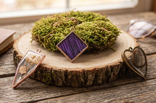 Rose gold and brass terrarium pendants featuring dried flowers, purple wood grain, and moss on a rustic wood slice.