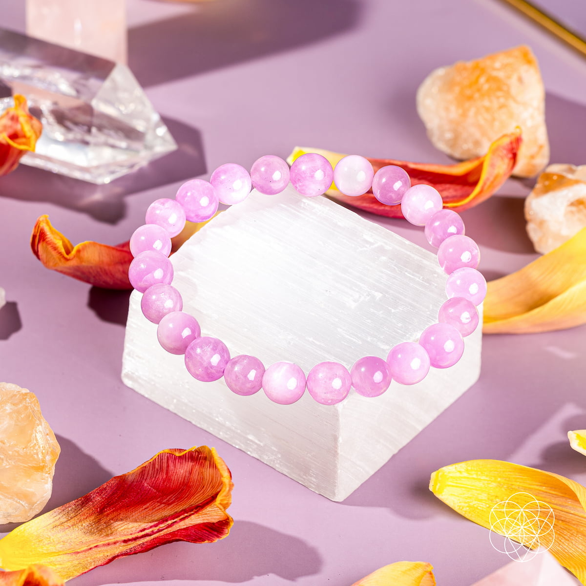 The Heart Reset - Rare Pink Kunzite Bracelet by Conscious Items rests on a white crystal, surrounded by vibrant petals and gemstones—a graceful piece celebrated for emotional healing and opening the heart.