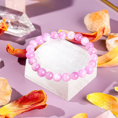 The Heart Reset - Rare Pink Kunzite Bracelet by Conscious Items rests on a white crystal, surrounded by vibrant petals and gemstones—a graceful piece celebrated for emotional healing and opening the heart.