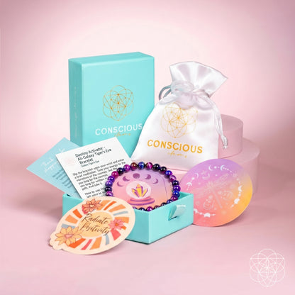 The Destiny Activator gift set by Conscious Items features a blue box, white pouch, All-Galaxy Tiger’s Eye 6mm bracelet, colorful cards, and a circular sticker—all beautifully displayed on a pink background with geometric patterns.