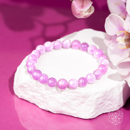 The Heart Reset - Rare Pink Kunzite Bracelet by Conscious Items rests on a white stone slab with white and pink flowers against a vibrant pink background—ideal for emotional healing and gently opening the heart.