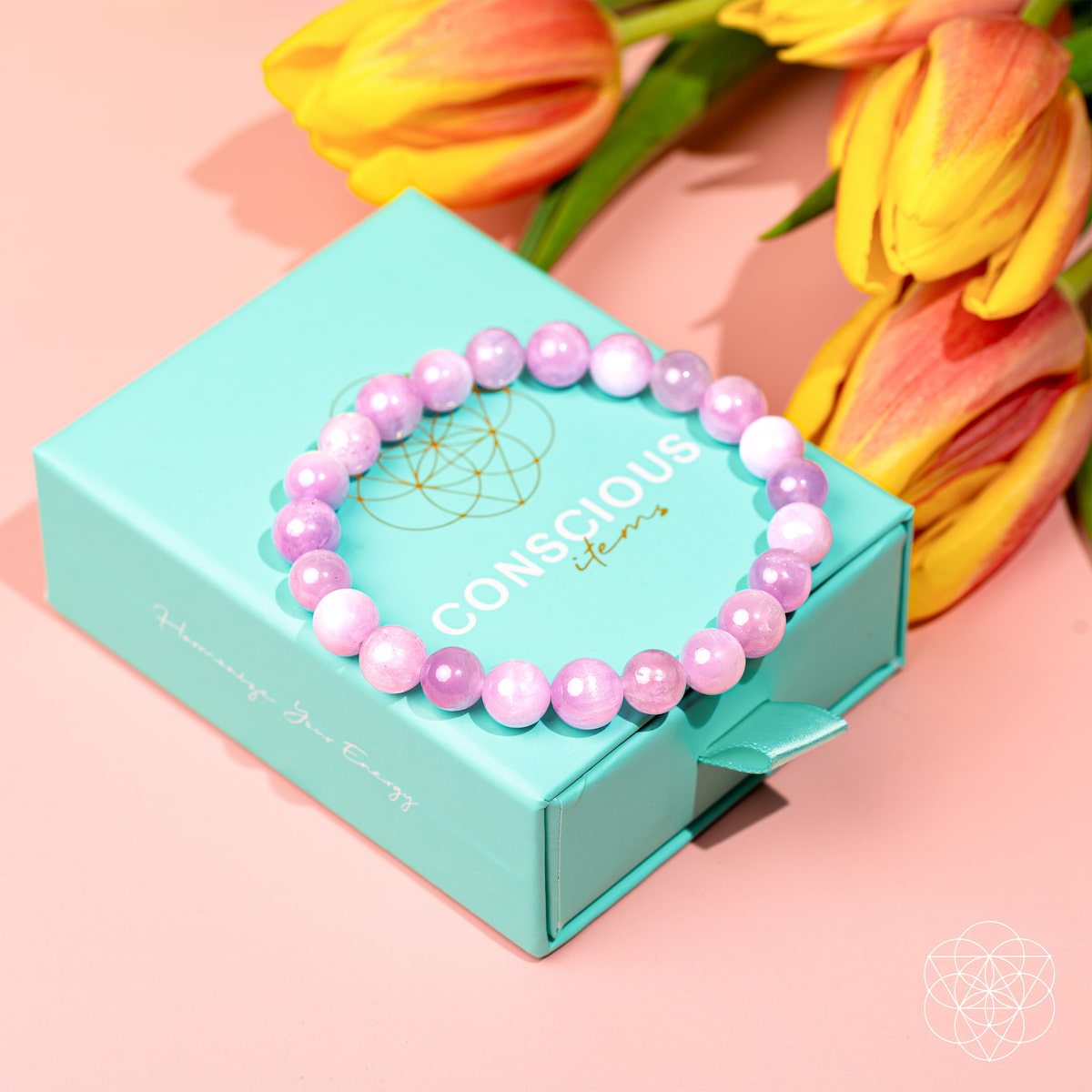 The Heart Reset - Rare Pink Kunzite Bracelet by Conscious Items rests on a turquoise gift box, accented by orange and yellow tulips in the background, all atop a light pink surface.