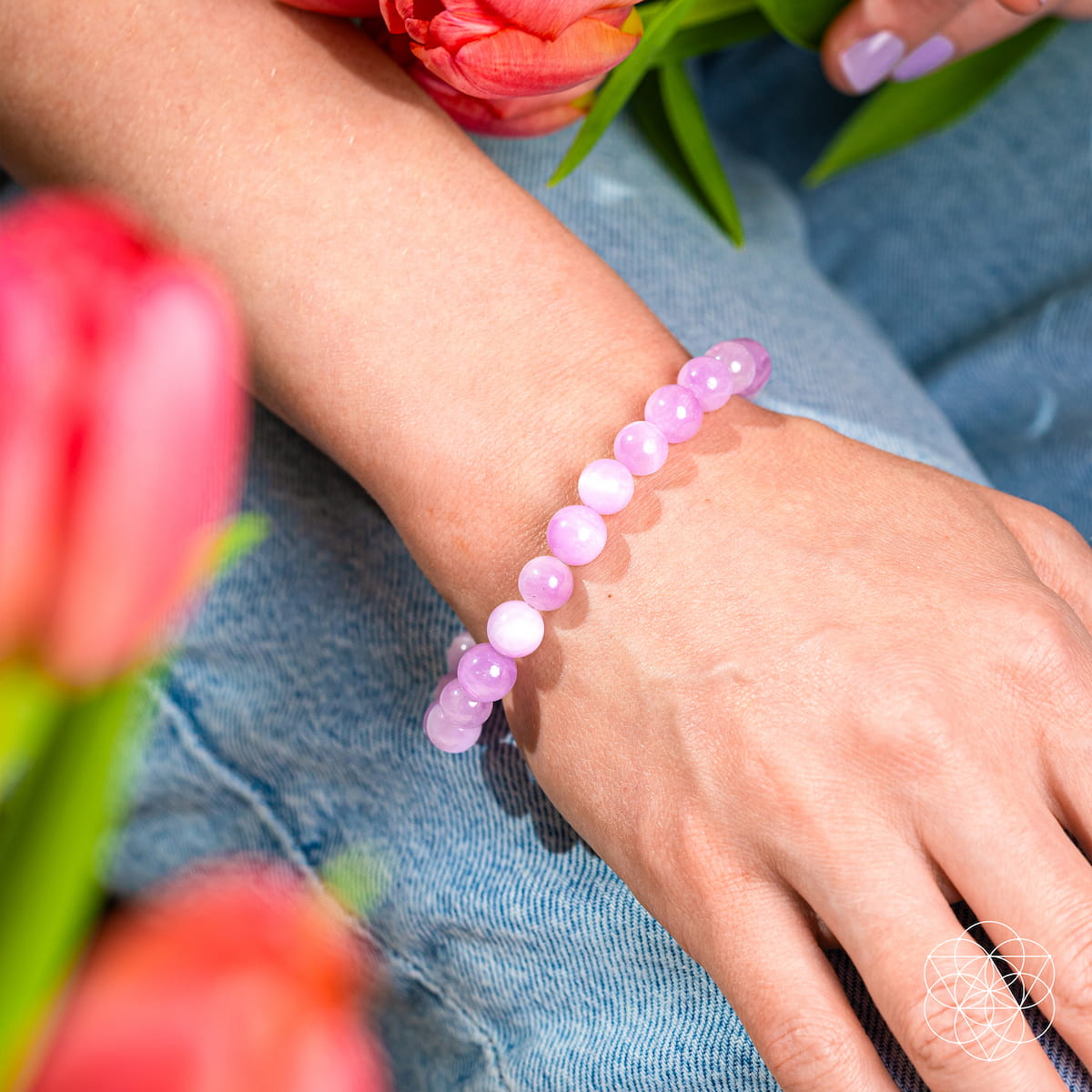 Someone wearing The Heart Reset - Rare Pink Kunzite Bracelet by Conscious Items—a gentle heart opener—on their wrist, dressed in blue jeans and surrounded by vivid orange tulips.