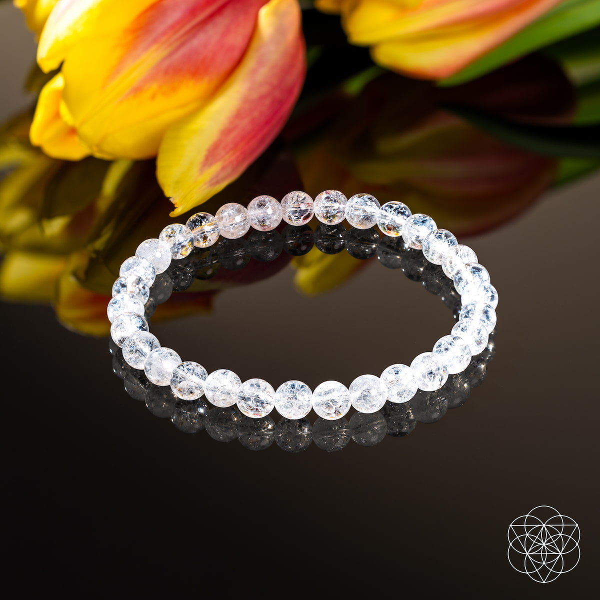 The Emotional Ice Bath – The Ice Quartz Bracelet | 6mm by Conscious Items rests on a glossy black surface, its reflection visible. Yellow and red tulips decorate the background, with a geometric white Conscious Items logo in the corner.
