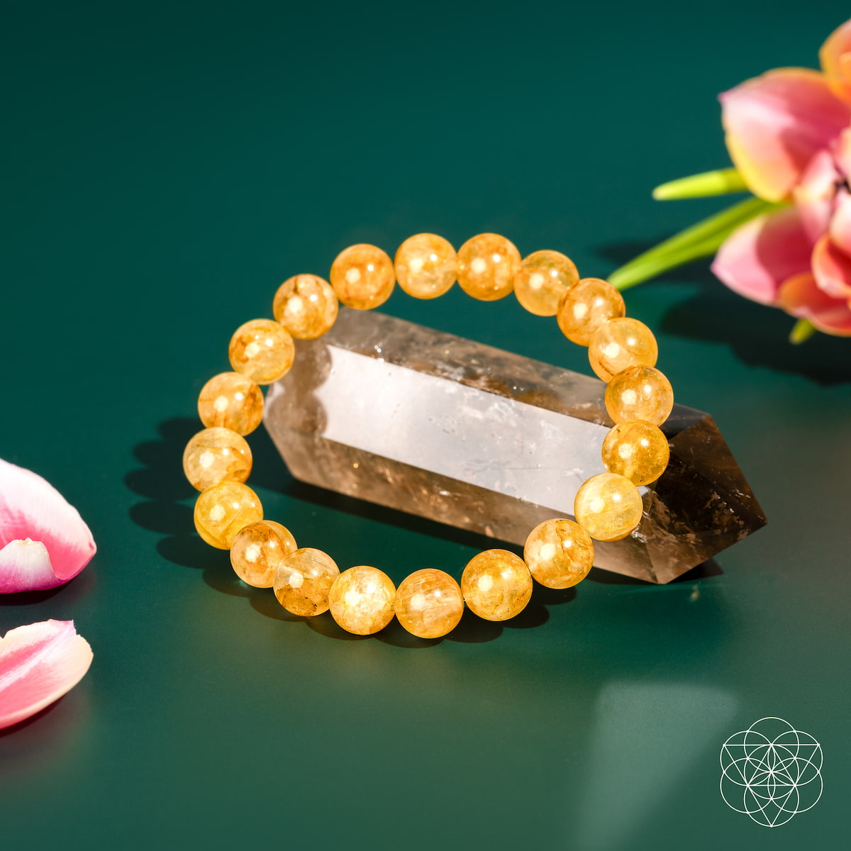 The Master Reset – Golden Healer Quartz Bracelet by Conscious Items rests on a polished crystal, surrounded by pink flowers on a green backdrop. A geometric white logo is visible in the corner.