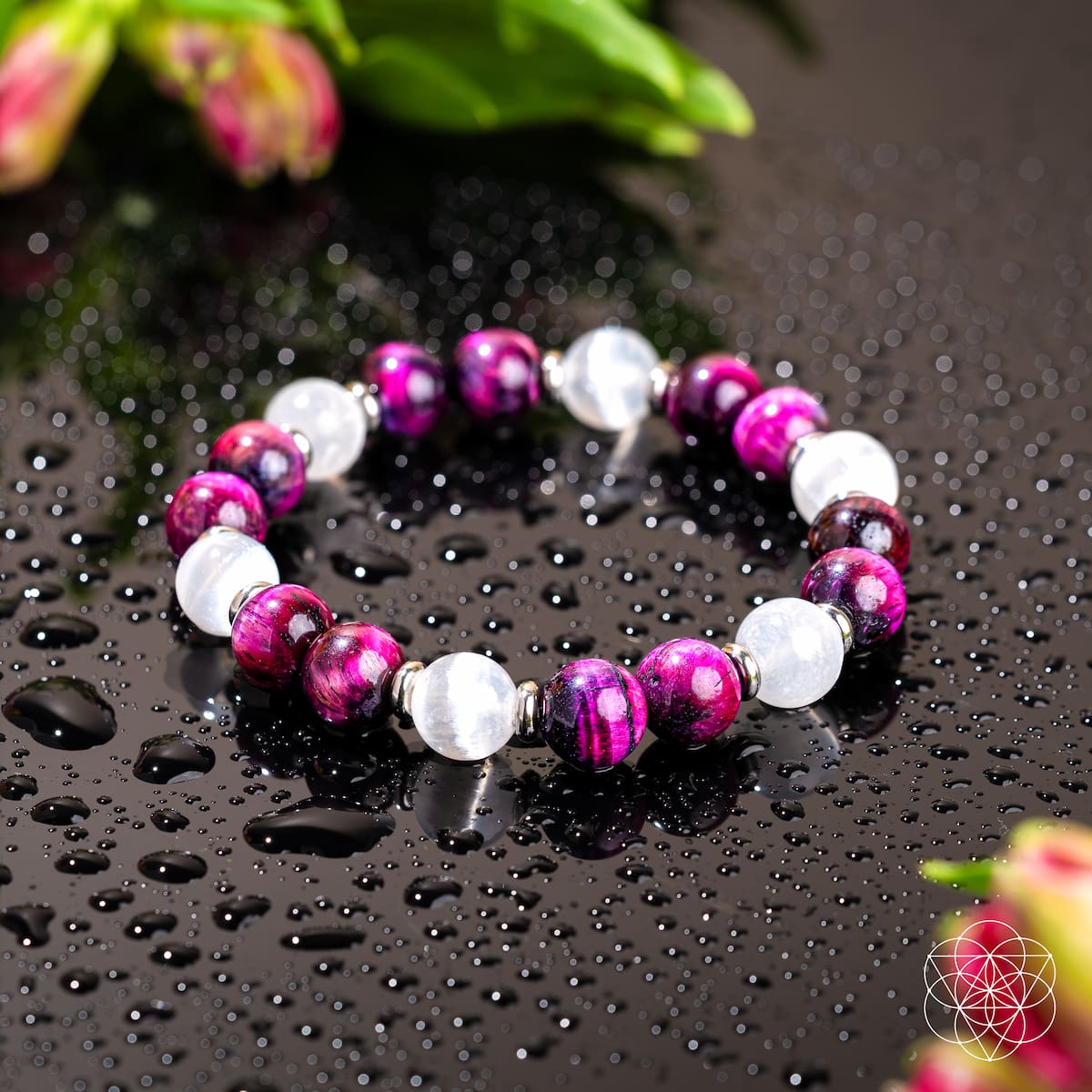 The Shape Your Future – Pink Galaxy Tiger’s Eye Bracelet by Conscious Items features alternating purple and white stones on a wet black surface, with water droplets and blurred green leaves and pink flowers in the background.
