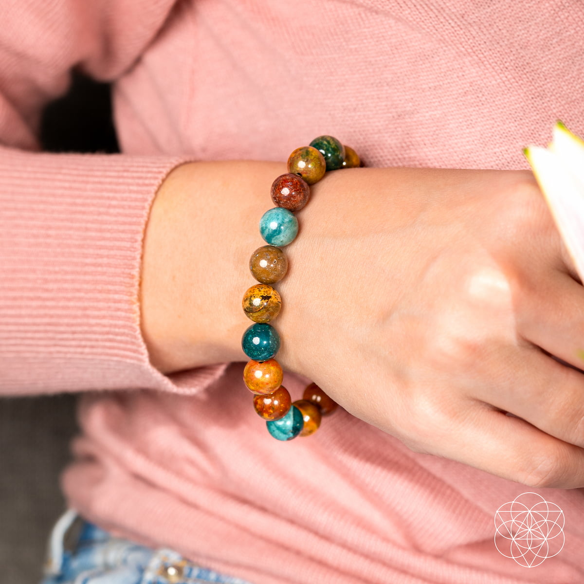 A person wears the Quiet My Mind – Ocean Jasper Bracelet by Conscious Items, featuring glossy Ocean Jasper beads in green, blue, yellow, and red for emotional balance.