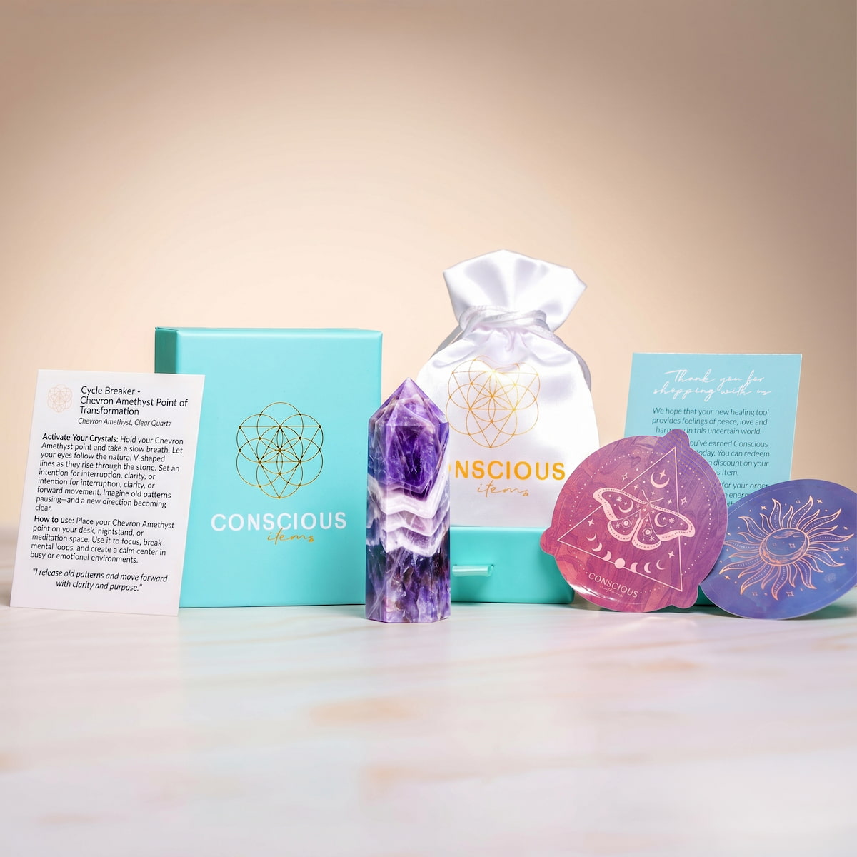 The Cycle Breaker - Chevron Amethyst Point of Transformation by Conscious Items includes a stress-relieving amethyst tower, blue box, white drawstring bag, two spiritual art cards, and an info card—all beautifully arranged on a light surface.