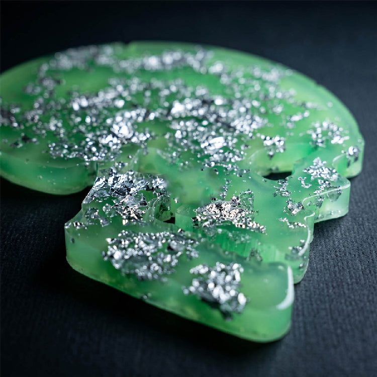 Green resin skull mold with silver metallic flakes on a dark background