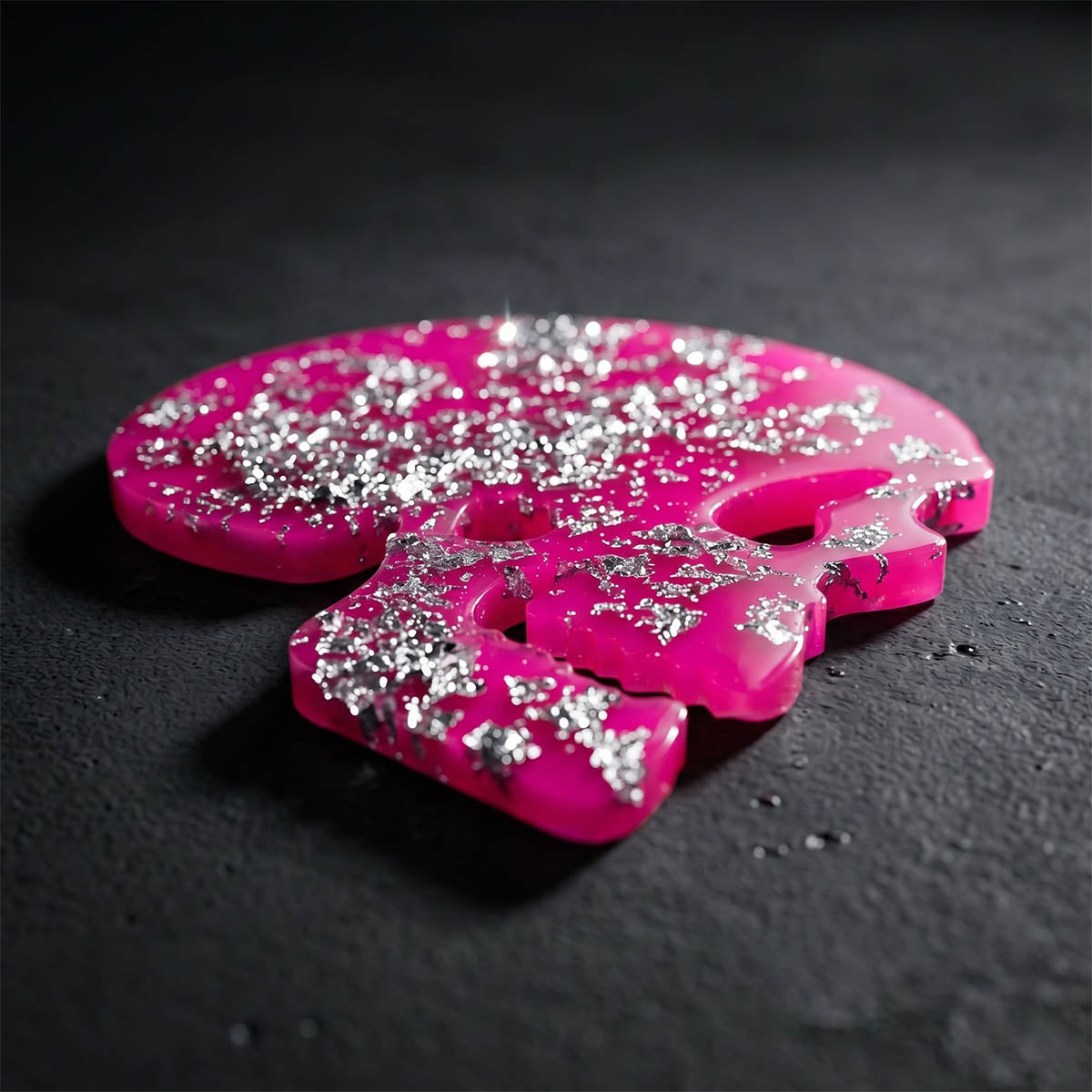 Pink and silver glittery skull coaster on a dark surface