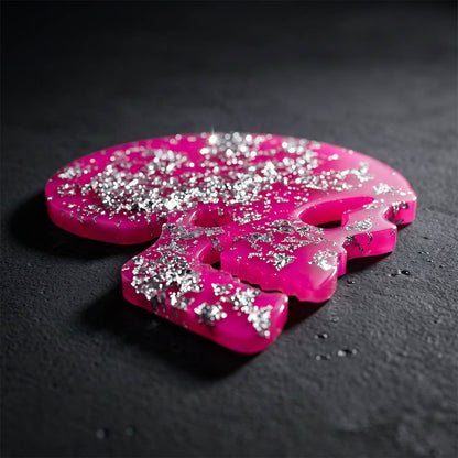 Pink and silver glittery skull coaster on a dark surface