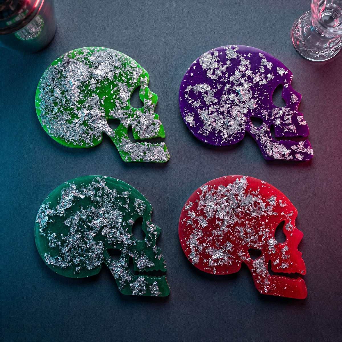 Four colorful skull coasters on a dark surface with 'The Memento Collection' branding.