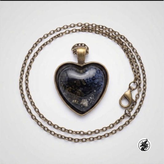 A heart-shaped glass pendant necklace with a dark blue and black marbled design inside, set in an antique bronze-toned metal frame, on a matching chain with a lobster clasp, photographed on a light gray background.