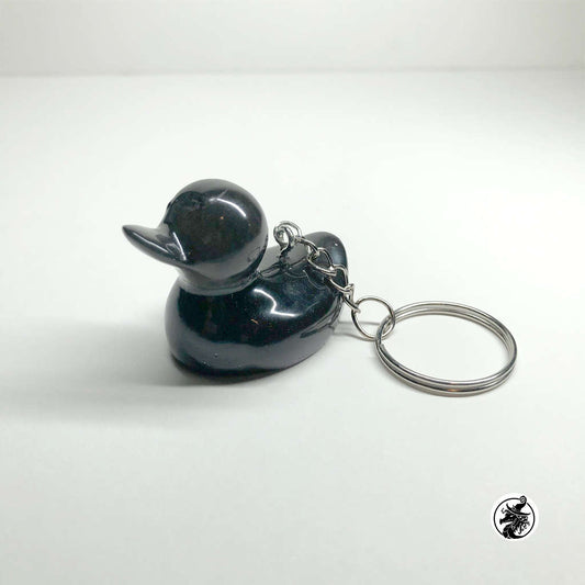Glossy black resin rubber duck keychain with subtle glitter particles, features a polished silver chain and split key ring, centered against a clean, light grey gradient background.
