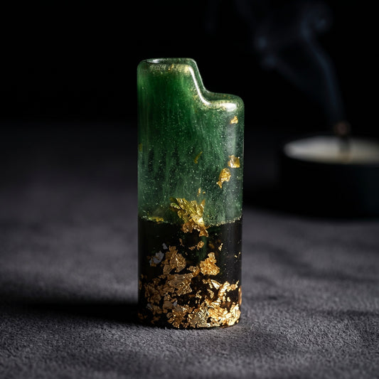 Handcrafted resin lighter case with emerald green swirls, a black base, and embedded gold leaf flakes on a metal pedestal.