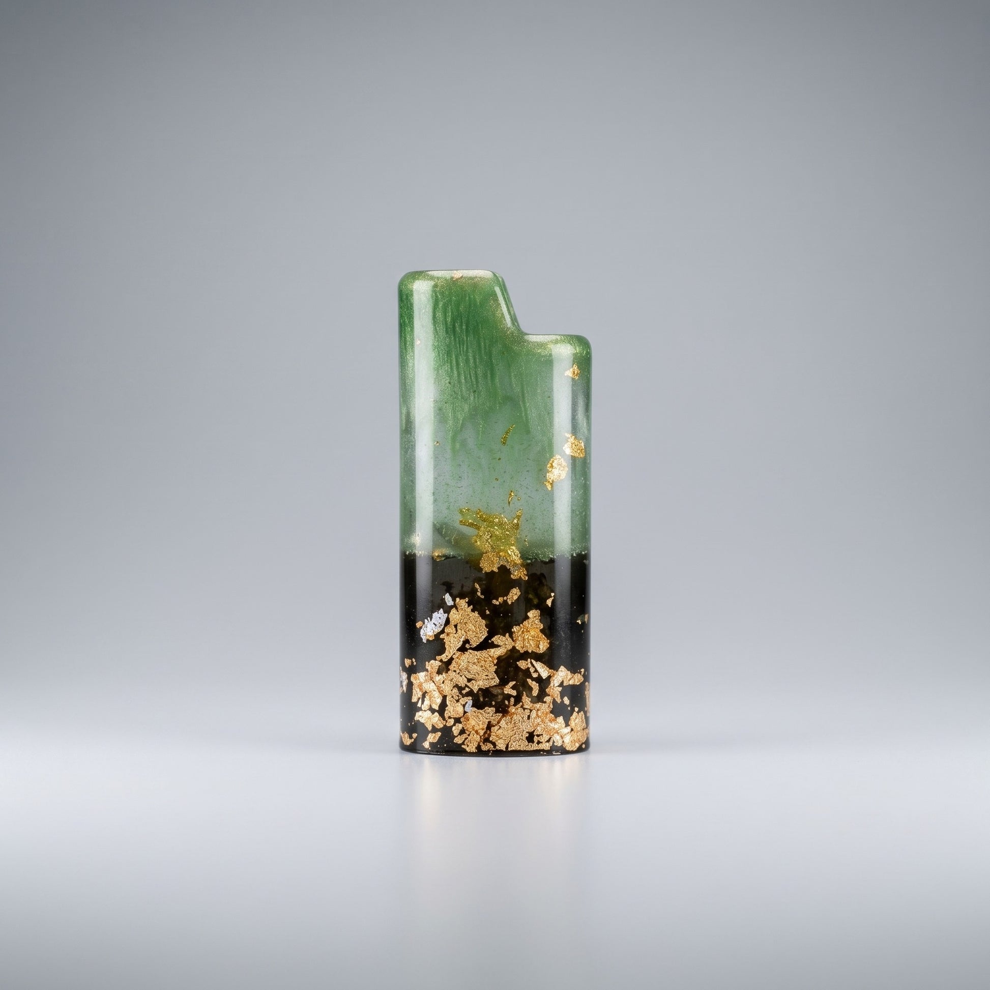 Handcrafted resin lighter case with emerald green swirls, a black base, and embedded gold leaf flakes on a metal pedestal.