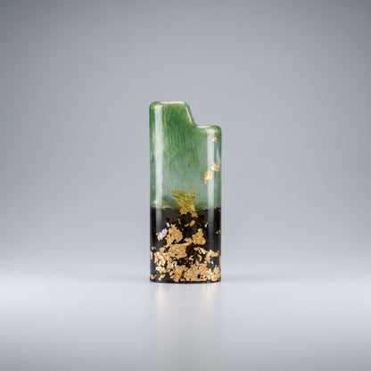 Handcrafted resin lighter case with emerald green swirls, a black base, and embedded gold leaf flakes on a metal pedestal.