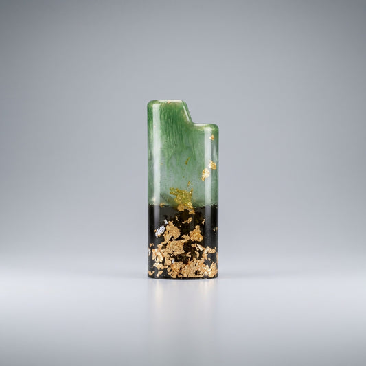 Handcrafted resin lighter case with emerald green swirls, a black base, and embedded gold leaf flakes on a metal pedestal.
