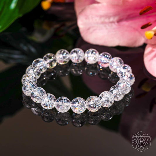 The Emotional Ice Bath – The Ice Quartz Bracelet by Conscious Items, known for emotional clarity, is displayed on a reflective black surface beside a pink flower, with soft lighting enhancing its sparkling beads.