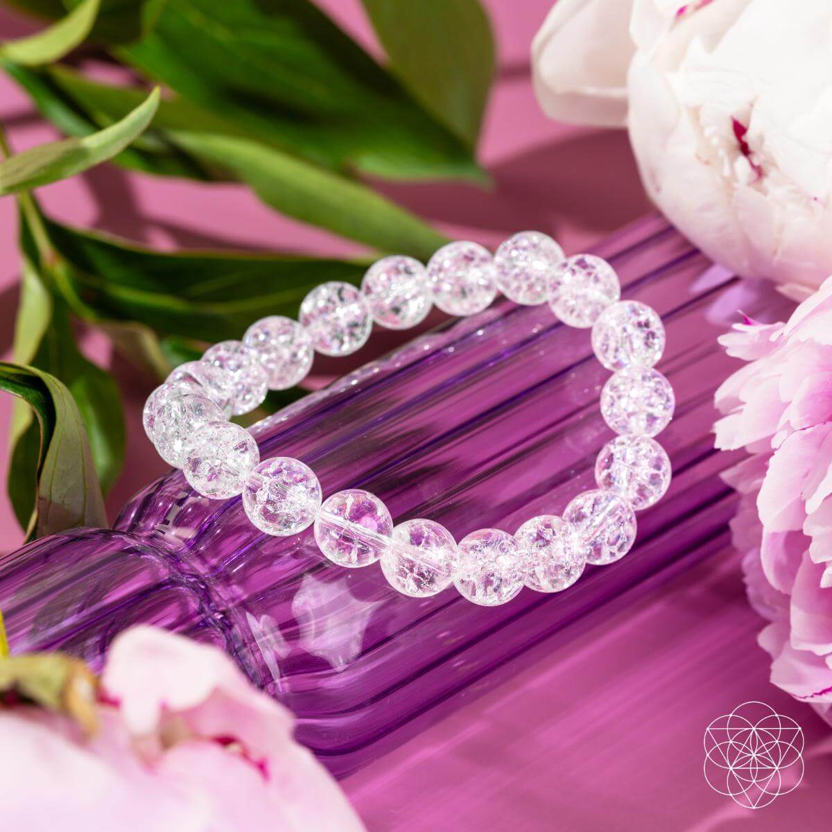 The Emotional Ice Bath – The Ice Quartz Bracelet by Conscious Items rests on a ribbed purple vase, surrounded by pink peonies and greenery, evoking emotional clarity. A geometric white logo appears in the bottom right corner.