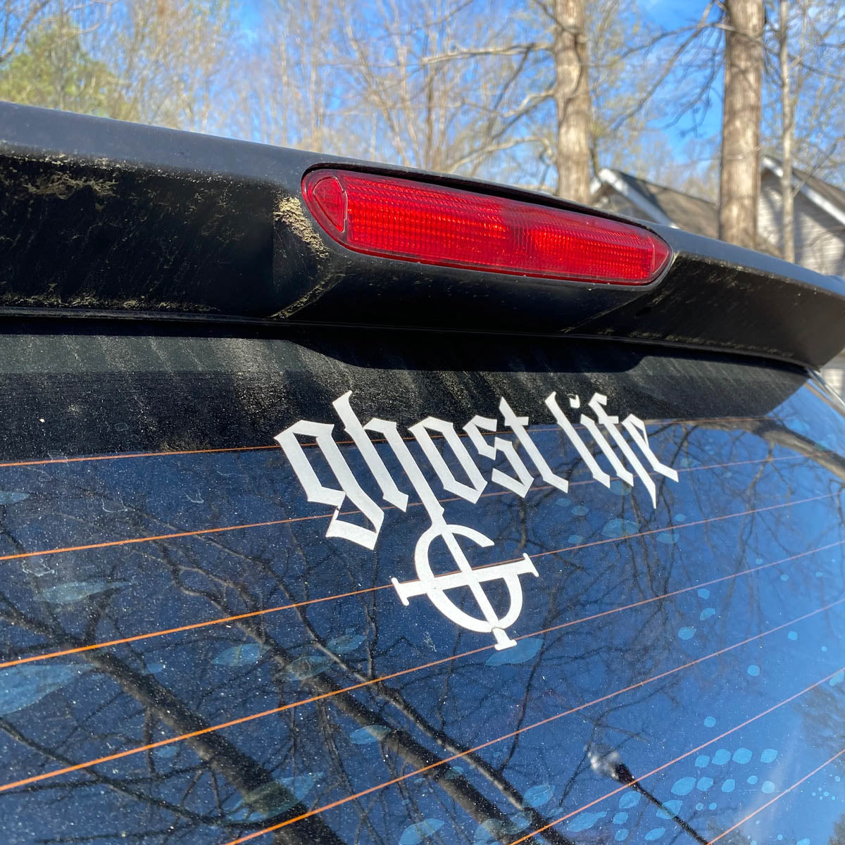Car window with 'ghost life' decal and reflection of trees and sky