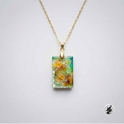 A gold chain necklace with a rectangular pendant featuring a green and yellow floral or mineral-like pattern, shown on a light gray background.