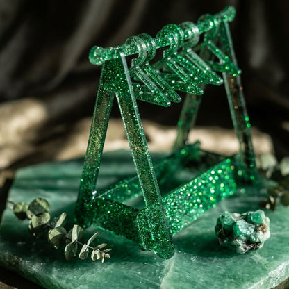 Green glittery sculpture resembling a bridge on a textured green surface with blurred background