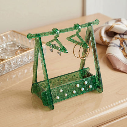 Green glittery jewelry stand with earrings on a wooden surface