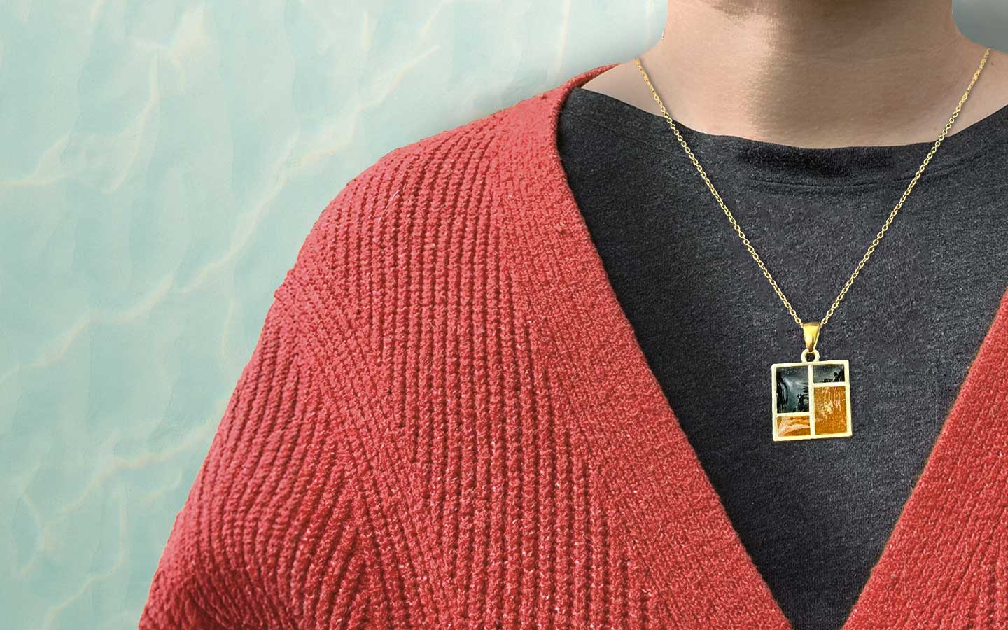 Person wearing a red sweater with a gold necklace featuring a square pendant.