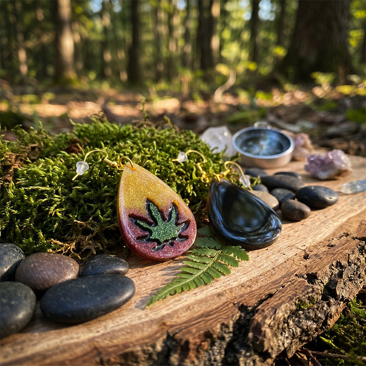 Earth-toned glitter resin earrings displayed on moss and wood in a sunlit forest setting with a compass.