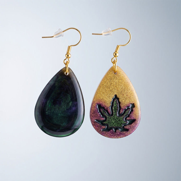 Pair of teardrop earrings: one with a gold and purple glitter leaf design, one with a dark green marbled finish.