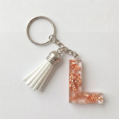 Keychain with a tassel and a decorative letter 'L' charm on a white background