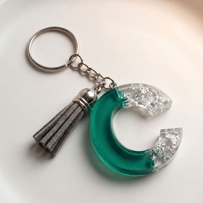 Keychain with green crescent moon design and tassel on a white background