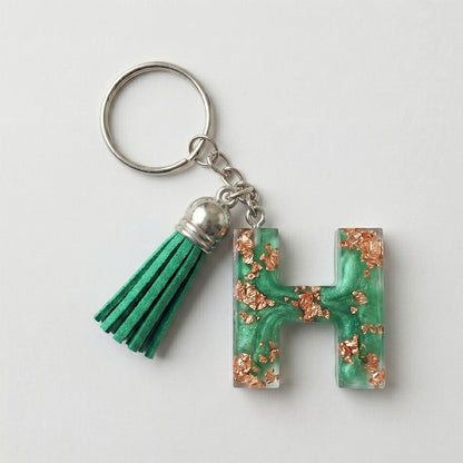 Keychain with green letter 'H' charm and tassel on a white background