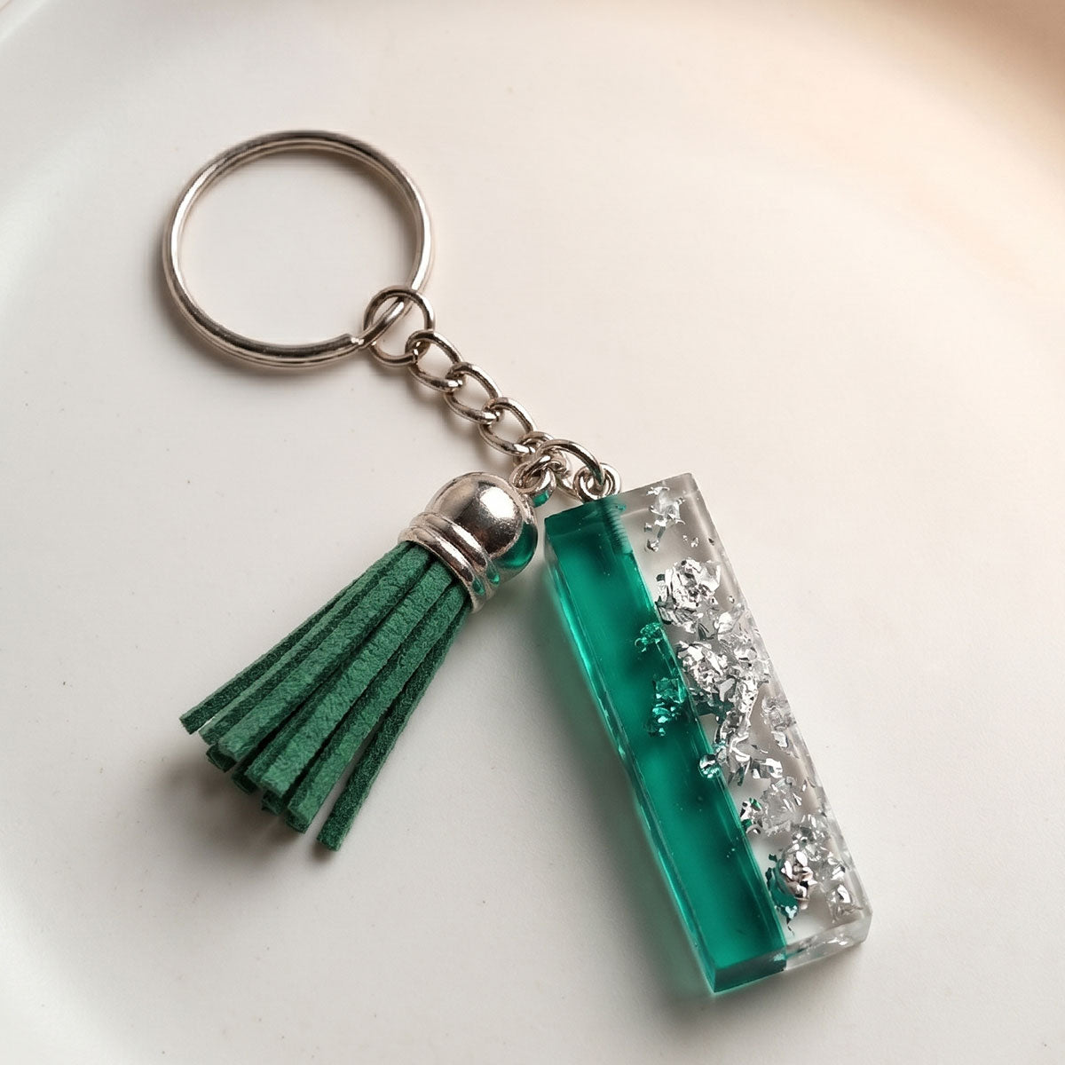 Keychain with 'I' teal resin charm and gray tassel on a light background