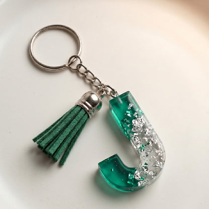 Keychain with green tassel and letter 'J' on a light background