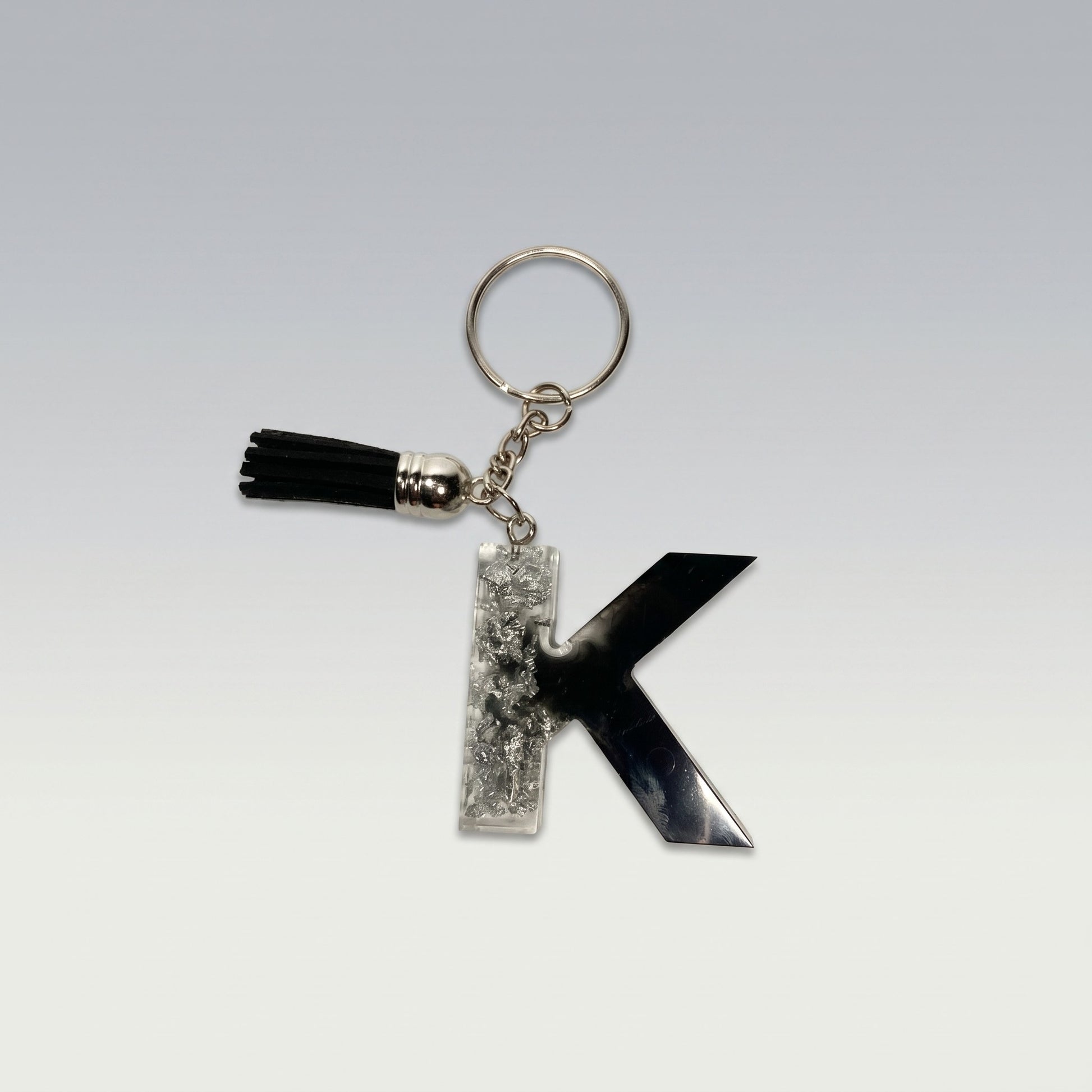 Resin black and silver keychain with letter 'K' and tassel on a light gray background