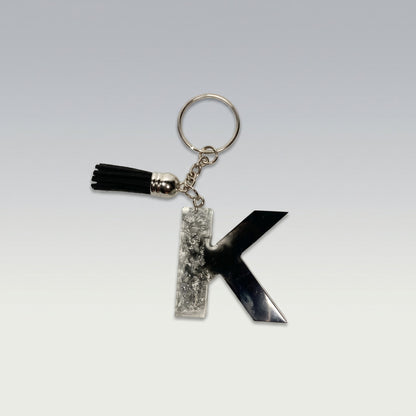 Resin black and silver keychain with letter 'K' and tassel on a light gray background