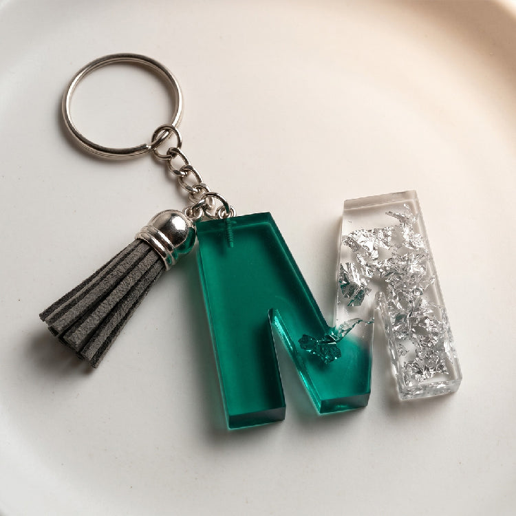 Keychain with green and clear rectangular charms and a gray tassel on a light background