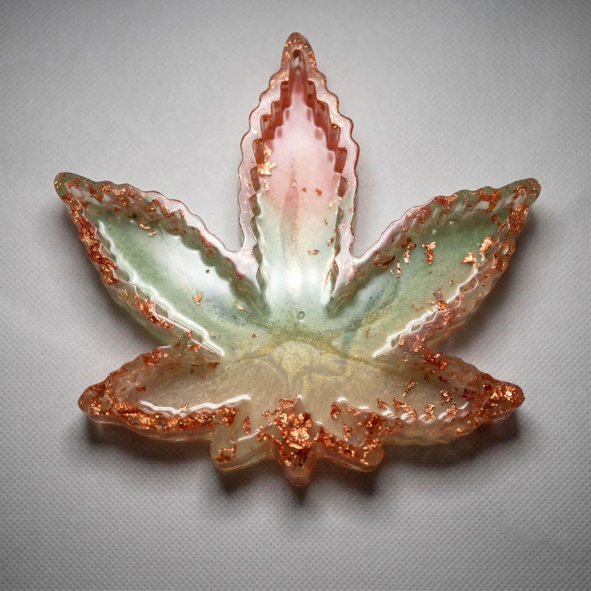 Cannabis leaf shaped resin ashtray with a green, peach, and gold gradient, featuring embedded copper foil flakes.