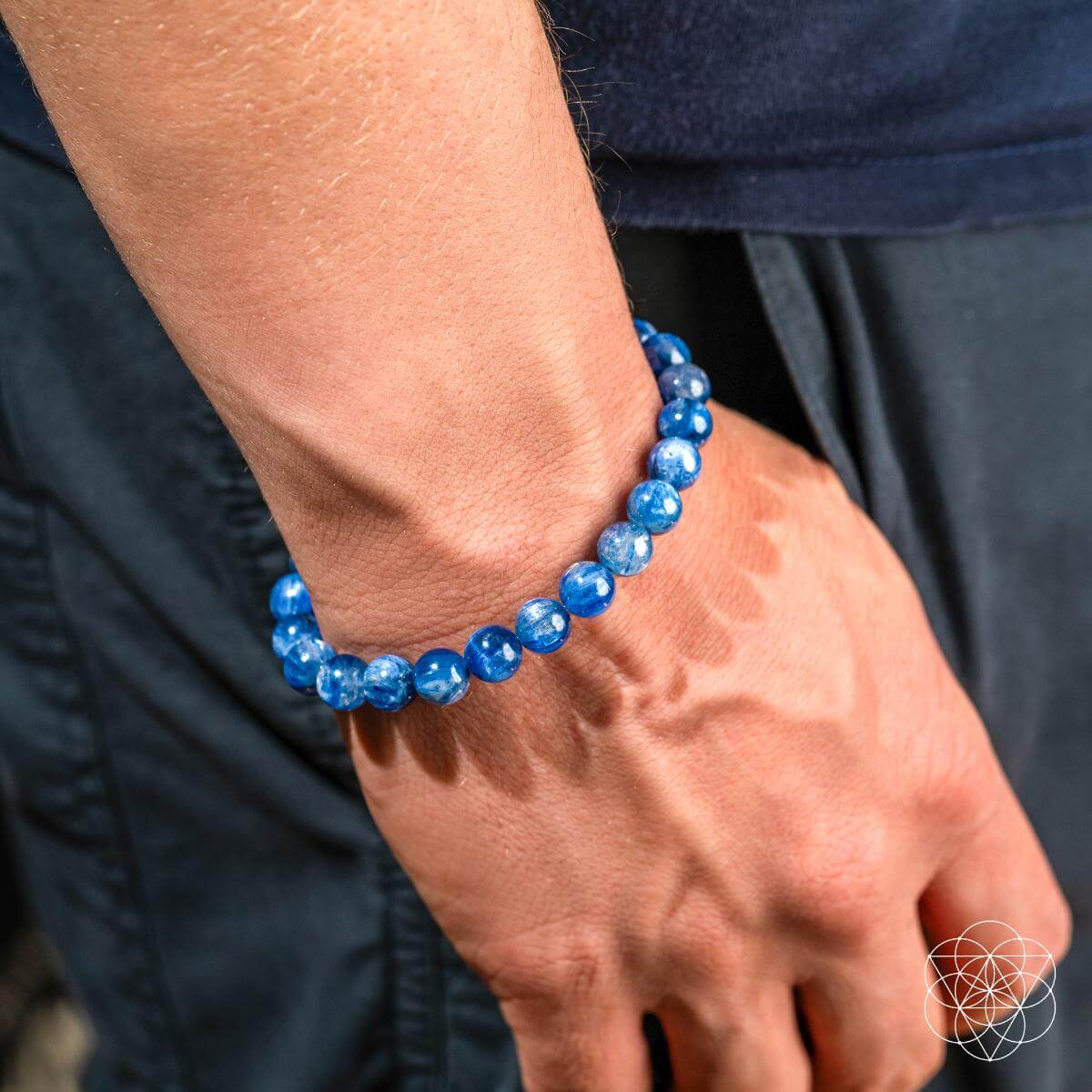 A person’s hand and wrist wear the My Truth, My Power – Rare Kyanite Bracelet by Conscious Items, paired with dark blue pants and a navy shirt—ideal for balancing the throat chakra.