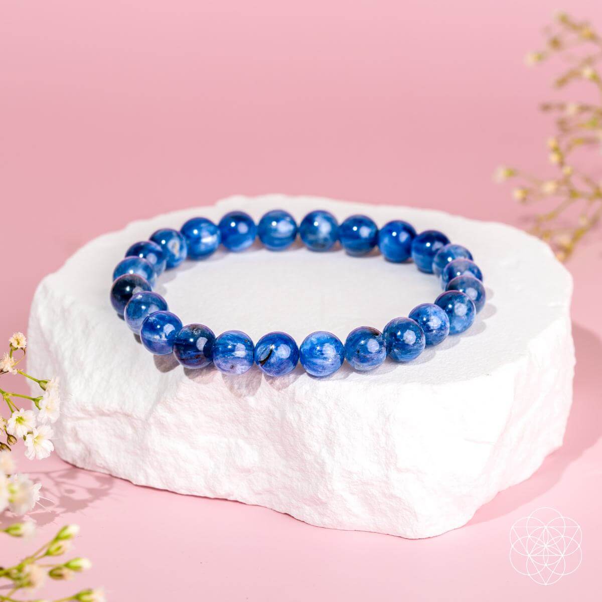 The "My Truth, My Power – Rare Kyanite Bracelet" by Conscious Items is showcased on a white stone platform with small white flowers and a pink backdrop—an ideal piece for throat chakra balance.