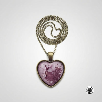 A heart-shaped pendant necklace with a purple and pink marbled or fluid-art pattern inside a bronze-toned bezel, suspended from an antique bronze chain on a light gray background.
